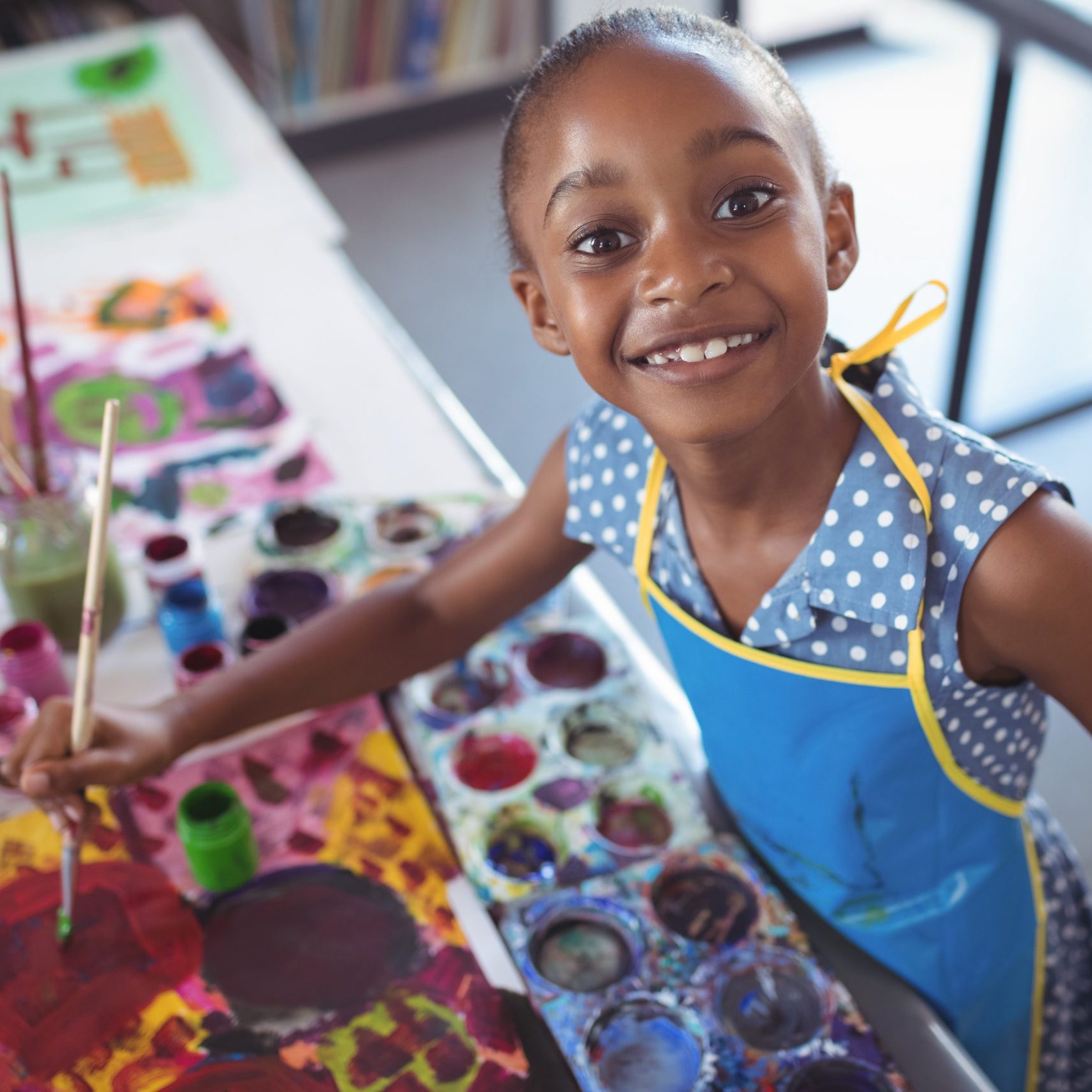 High angle portrait of elementary girl painting at desk in classroom